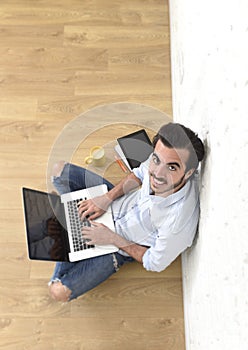 Young man in hipster modern casual style look sitting on living room home floor working on laptop