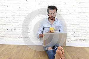 Young man in hipster modern casual style look sitting on living room home floor working on laptop