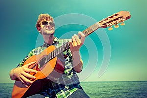 Young man hipster playing guitar by sea ocean.