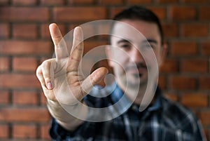 Young man in his 30s showing three fingers. Selective focus