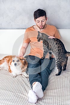 Young man with his dog and cat is hugging on the bed. Pets