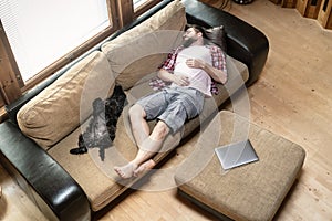 Young man with his dog Schnauzer amusingly fell asleep on a soft sofa, next to a laptop