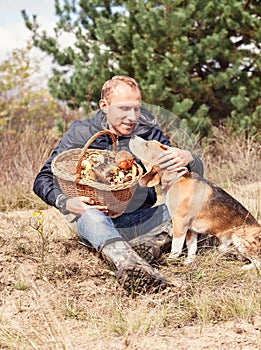 Young man with his dog on sunny autumn forest glade with mushroo