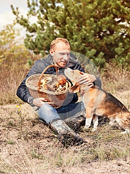 Young man with his dog on sunny autumn forest glade with mushrooms