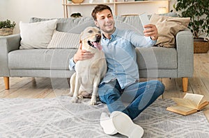 Young man with his dog taking selfie at home