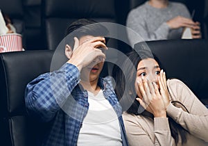 Young man with his girlfriend closing faces in terror while watching horror movie in cinema