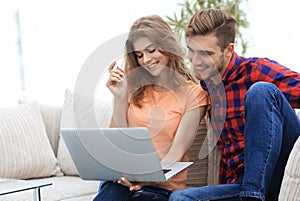 Young man with his girlfriend watching a TV show on the laptop sitting in the living room