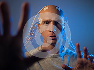 A young man with his head entangled in wires, pulls his hands forward,
