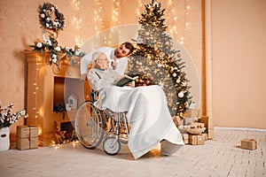 Young man and his old father on a wheelchair sitting near Christmas tree