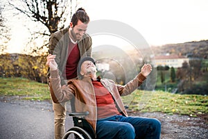 Young man and his senior father in wheelchair on a walk in town.