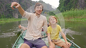 A young man and his son on a boat having a river trip among spectacular limestone rocks in Ninh Binh, a tourist