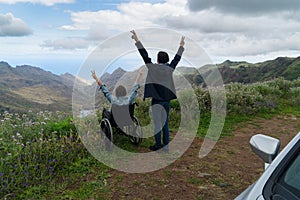 Young man and his wife in wheelchair travelling together by car in mountains