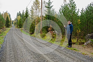 Young man hitchhiking on a finnish country road near the woods