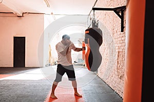 A young man is hitting a punching bag in the gym. The athlete is engaged in boxing. The sportsman is training
