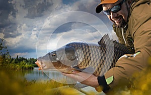 Young man hold big carp in his hands.