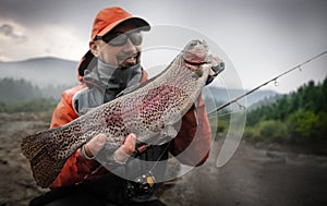 Young man hold big rainbow trout in his hands.