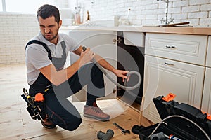 Young man hold hose in hand. Bad smell. Stinks. Handyman suffer from it. Opened toolbox and piece of pipe on floor.