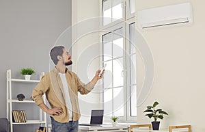 Young man holding air conditioner remote control and adjusting temperature at home