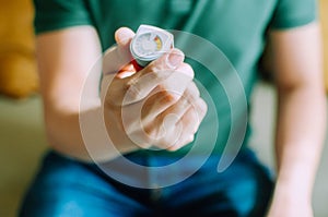 A young man is holding an asthma inhaler device while sitting on a couch