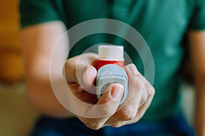 A young man is holding an asthma inhaler device while sitting on a couch