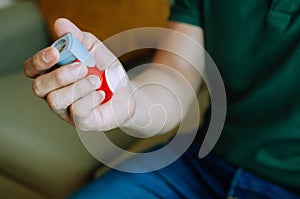 A young man is holding an asthma inhaler device while sitting on a couch