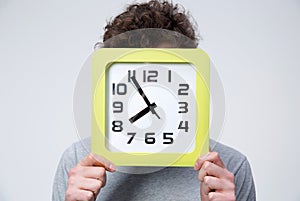 Young man holding a big clock covering his face