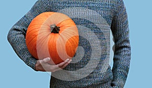 Young man holding a big heavy orange pumpkin in his hands on a blue background, halloween concept
