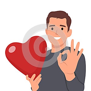 Young man holding big love red heart with ok sign. Valentine day concept