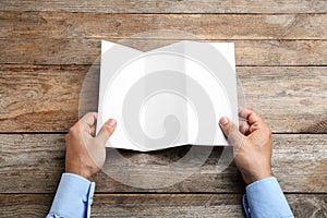 Young man holding blank brochure at  table, top view. Mock up for design