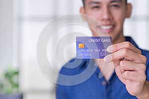 Young man holding a blue credit card prepare for shopping online. Space for text. Selective focus. Payment and e-commerce concept