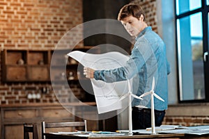 Young man holding blueprint and looking at wind turbines