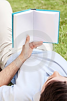 Young man holding book while lying in park photo
