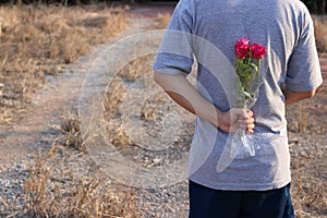 Young man is holding a bouquet of beautiful red roses in his back on countryside blurred background. Romance dating or Valenday`s