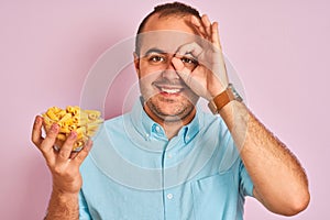 Young man holding bowl with macaroni pasta standing over isolated pink background with happy face smiling doing ok sign with hand