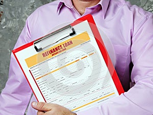 Young man holding a business paper in hands. Conceptual photo about REFINANCE LOAN Application Form with written text