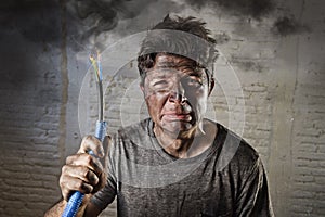 Young man holding cable smoking after electrical accident with dirty burnt face in funny sad expression