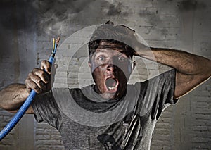 Young man holding cable smoking after electrical accident with dirty burnt face in funny sad expression