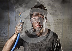 Young man holding cable smoking after electrical accident with dirty burnt face in funny sad expression