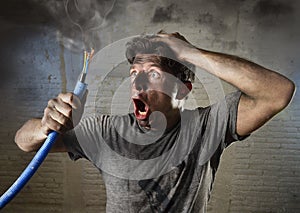 Young man holding cable smoking after electrical accident with dirty burnt face in funny sad expression