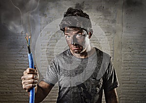 Young man holding cable smoking after electrical accident with dirty burnt face in funny sad expression