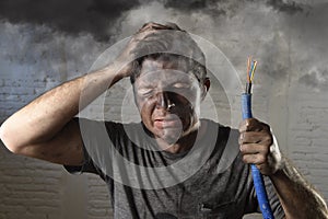 Young man holding cable smoking after electrical accident with dirty burnt face in funny sad expression