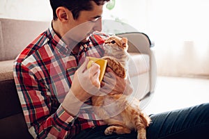 Young man holding a cat and drinking tea at home