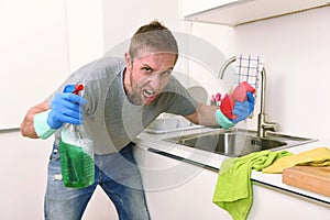 Young man holding cleaning detergent spray and sponge washing home kitchen clean angry in stress