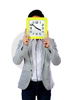 Young man holding clock covering his face