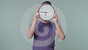 Young man holding clock watch, hiding, checking time on clock, running late to work being in delay