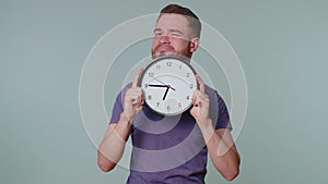 Young man holding clock watch, hiding, checking time on clock, running late to work being in delay