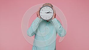 Young man holding clock watch, hiding, checking time on clock, running late to work being in delay