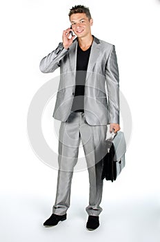 Young man with briefcase and cell phone standing against white background