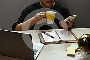 Young man holding coffee cup and using smart phone.