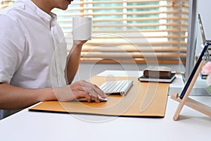 Young man holding coffee cup and working online at home office.